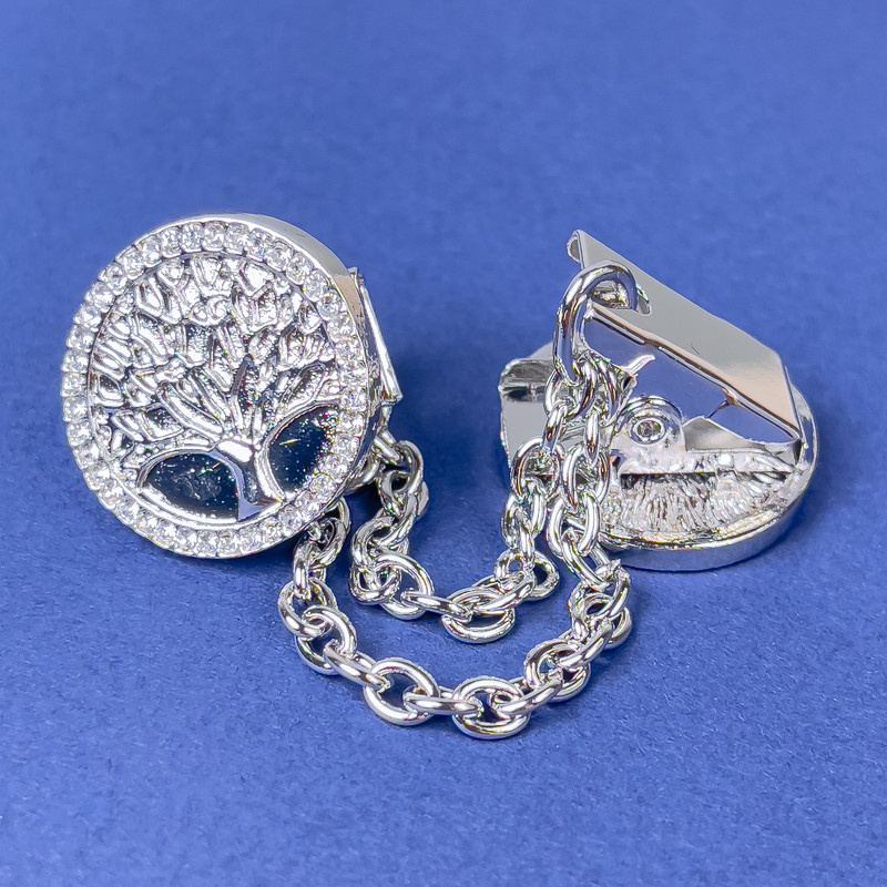 Srebrzysta broszka z zaciskiem do kardiganów, metal srebrzysty i białe cyrkonie, średnica ok. 20 mm, łańcuszek długości ok. 9 cm