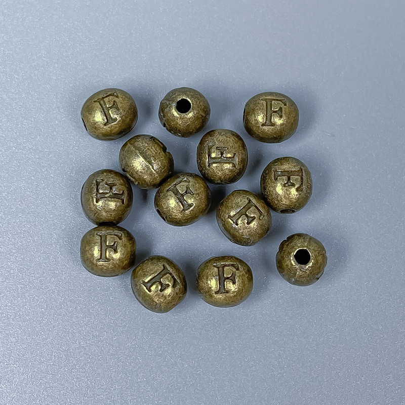 Koralik-wstawka z literą „F” w kolorze starego brązu, średnica 6×7 mm ±, otwór 1,8 mm ±, opakowanie 28 szt.