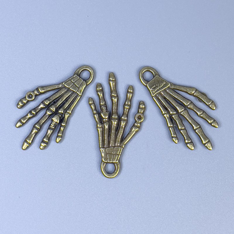Zawieszka dłoni szkieletu, kolor brązowy, wymiary 35×19×2 mm ± otwór, średnica 3 mm ± opakowanie 20 g (~9 szt.)