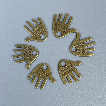 Zawieszka w formie dłoni, brązowy kolor metalu, rękodzieło, wymiary 12×11×1 mm ± otwór, średnica 1,5 mm ± opakowanie 20 g (~50 szt.)