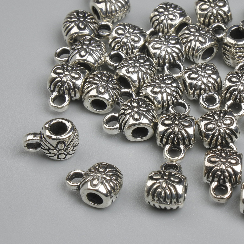 Zawieszka bail w kolorze metalu srebrzystym, wymiary 8×4,5 mm +/- otwory Ø 2 mm +/- Ø 3 mm +/- opakowanie 26 szt.