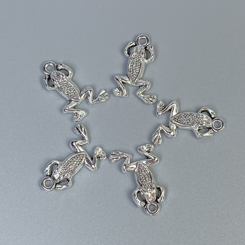 Zawieszka biżuteryjna Żabka, kolor metalu: srebrny, wymiary 20×13×3 mm ± otwór Ø 1,5 mm ± opakowanie 20 g (~18 szt.)