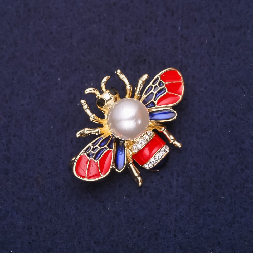 Broszka Pszczoła z perłową koraliką, emalią i kryształkami, kolor czerwony, niebieski i biały, 35×25 mm, metal złocisty