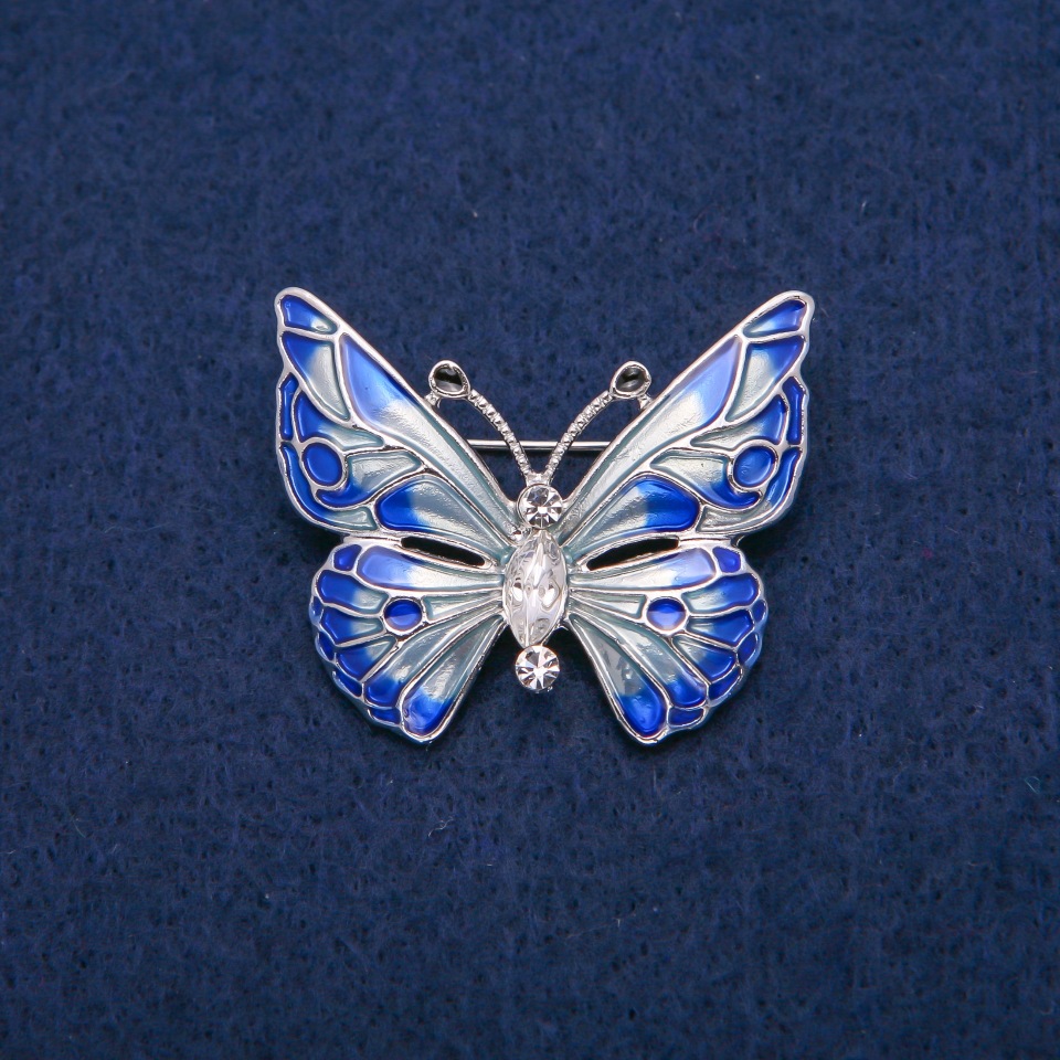 Broszka motyl z białymi kryształami i błękitną emalią, złocisty metal 31 × 37 mm