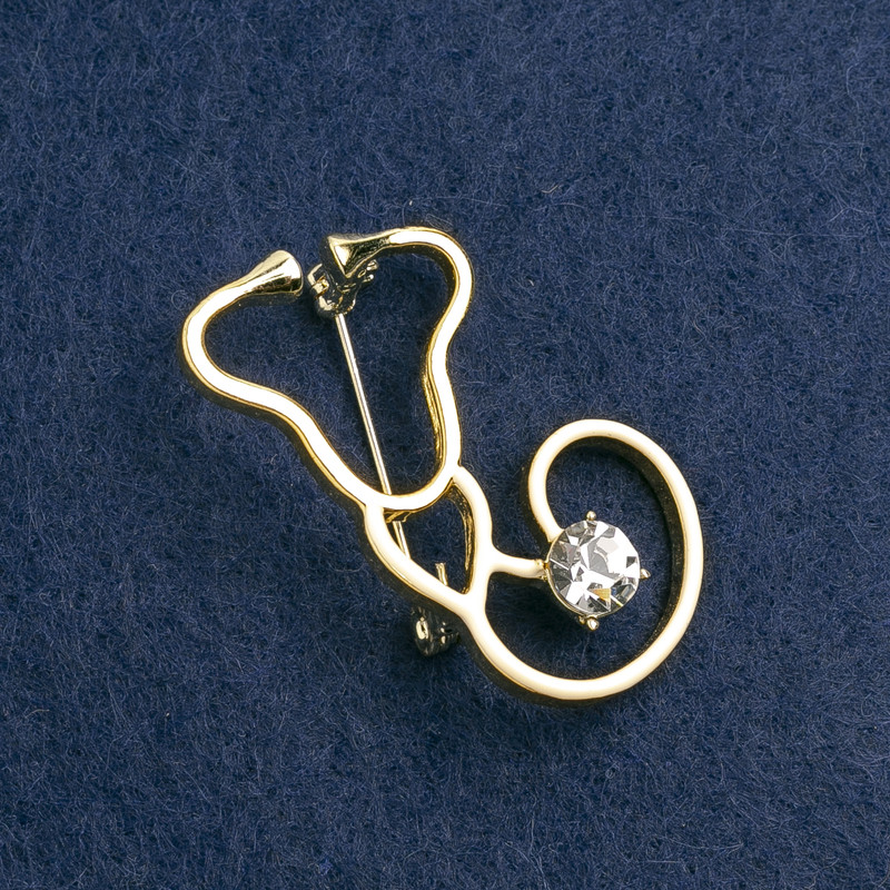 Broszka w formie stetoskopu, z emalią białą, z białym kamieniem, metal złoty 42×25 mm