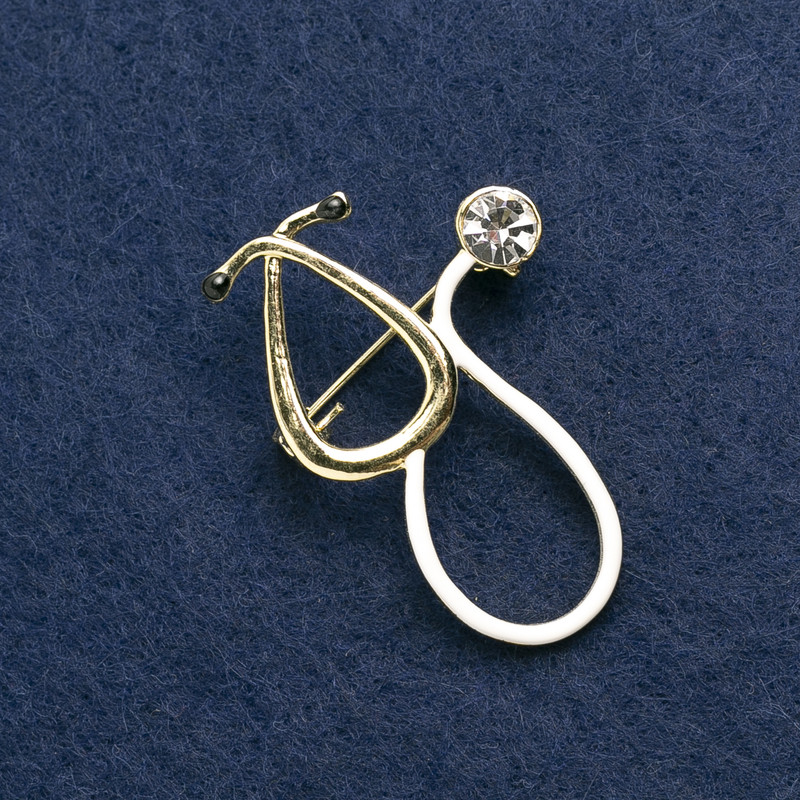 Broszka ze stetoskopem, emalia biała, z białym kamieniem, metal złocisty 43×29 mm